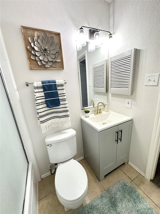 bathroom featuring vanity, a shower with door, toilet, baseboards, and tile patterned floors