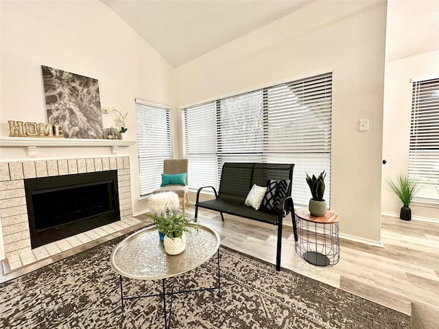 living area with baseboards, a brick fireplace, wood finished floors, and vaulted ceiling