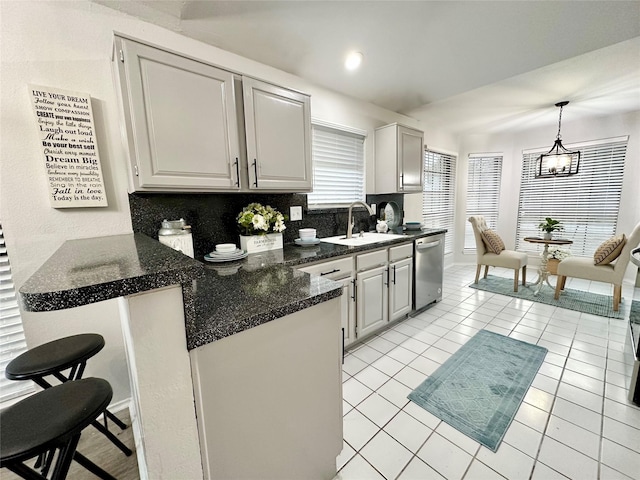 kitchen with backsplash, decorative light fixtures, stainless steel dishwasher, a sink, and a peninsula