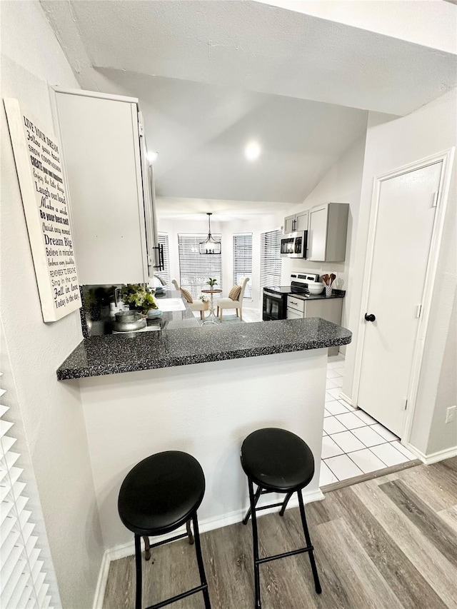 kitchen with dark countertops, appliances with stainless steel finishes, light wood finished floors, a breakfast bar area, and a peninsula