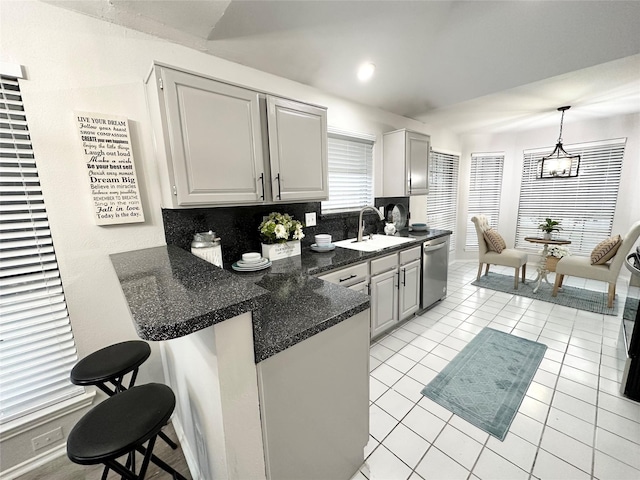 kitchen featuring light tile patterned flooring, a sink, dishwasher, a kitchen breakfast bar, and a peninsula