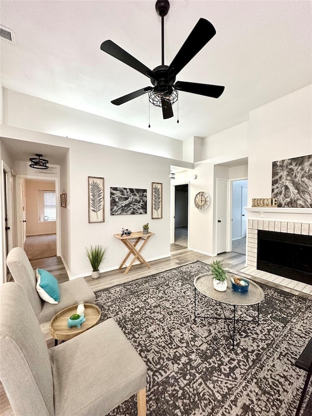 living area with visible vents, wood finished floors, a fireplace, baseboards, and a ceiling fan