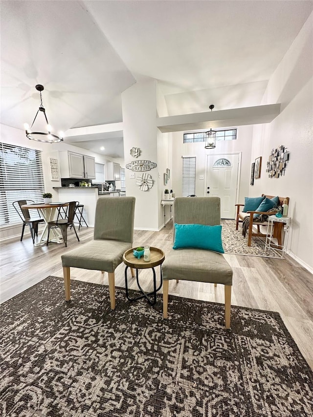 living area featuring vaulted ceiling, an inviting chandelier, baseboards, and light wood finished floors
