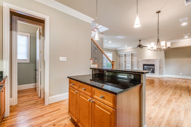 kitchen featuring light wood-type flooring, a fireplace with raised hearth, ceiling fan with notable chandelier, and ornamental molding