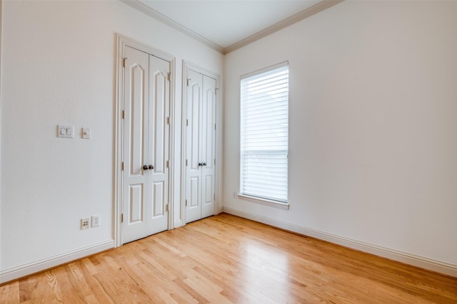 unfurnished bedroom featuring multiple closets, baseboards, ornamental molding, and wood finished floors