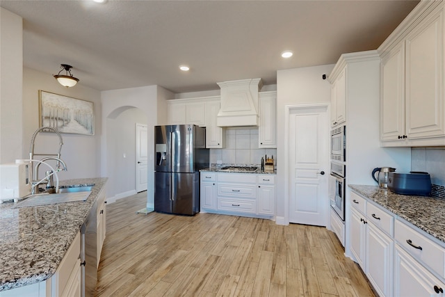 kitchen featuring custom range hood, light wood finished floors, white cabinets, and stainless steel appliances