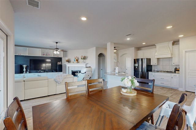 dining room with arched walkways, a tiled fireplace, light wood-style flooring, a ceiling fan, and visible vents