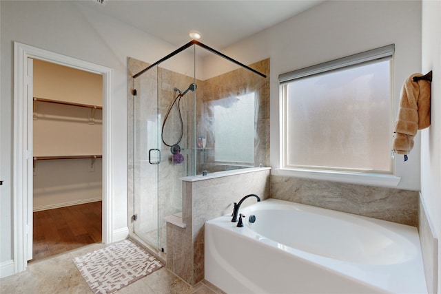 full bathroom featuring a spacious closet, a garden tub, and a stall shower
