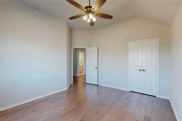 unfurnished bedroom with baseboards, wood finished floors, lofted ceiling, visible vents, and a closet