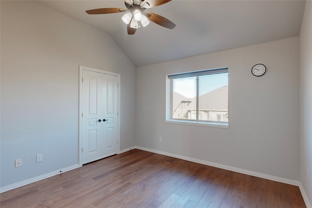 unfurnished bedroom featuring a closet, lofted ceiling, wood finished floors, baseboards, and ceiling fan