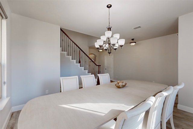 dining room with visible vents, baseboards, a chandelier, stairs, and light wood-style flooring