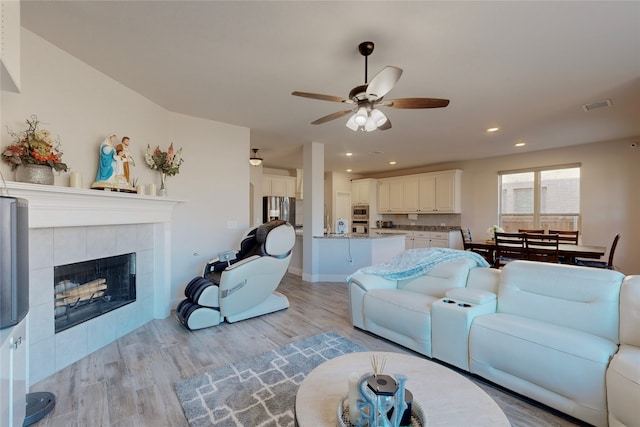 living area featuring a ceiling fan, visible vents, a tiled fireplace, light wood-style floors, and recessed lighting