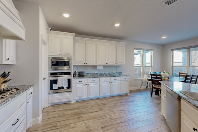 kitchen with visible vents, baseboards, light stone counters, light wood finished floors, and stainless steel appliances