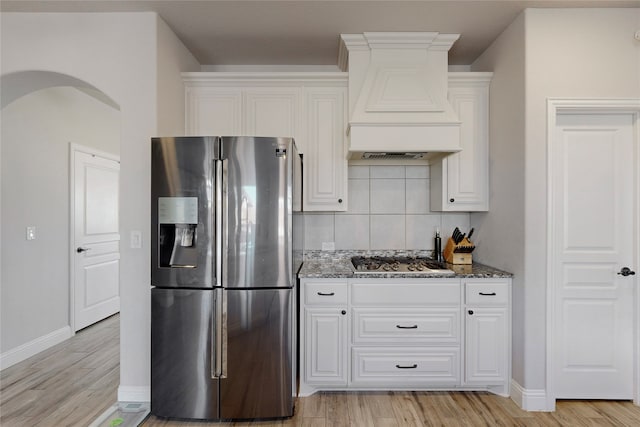 kitchen with premium range hood, dark stone countertops, stainless steel appliances, decorative backsplash, and light wood-type flooring