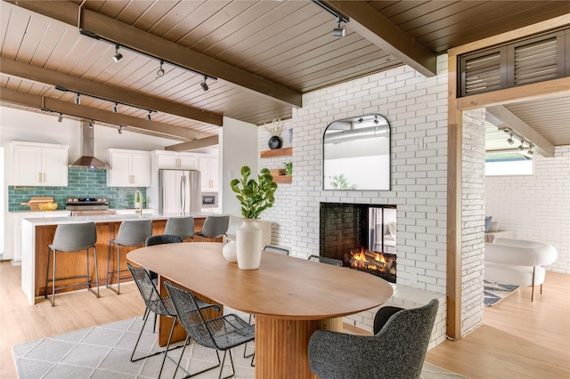 dining room with wood ceiling, brick wall, a brick fireplace, track lighting, and light wood-style floors