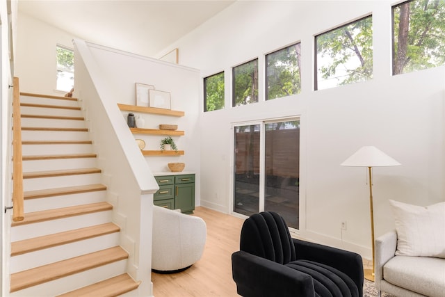 living area with stairs, a high ceiling, and light wood-style floors