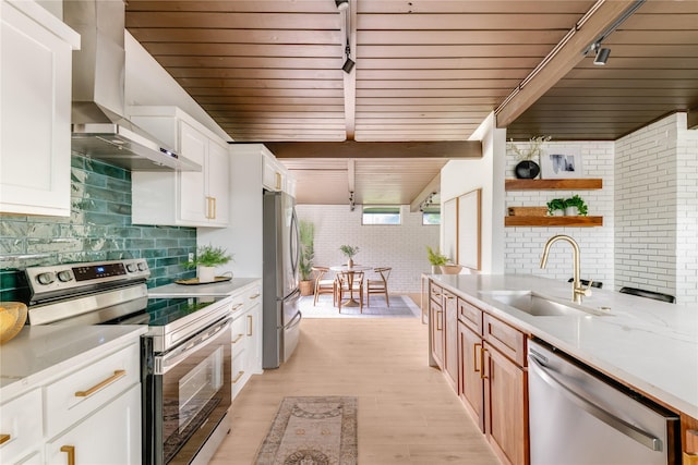 kitchen featuring wall chimney range hood, open shelves, a sink, light countertops, and stainless steel appliances
