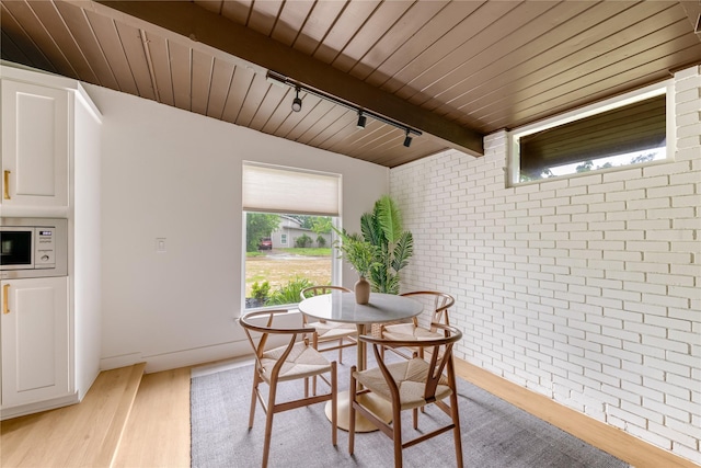 dining room with track lighting, wooden ceiling, brick wall, and light wood-style flooring