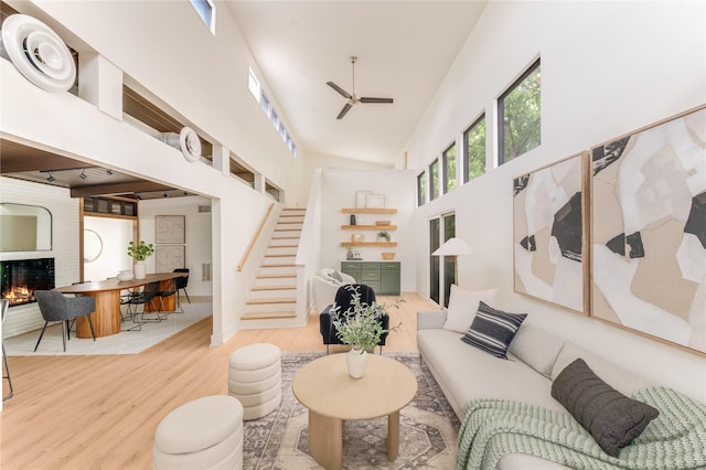 living room with a fireplace, a ceiling fan, wood finished floors, a towering ceiling, and stairway