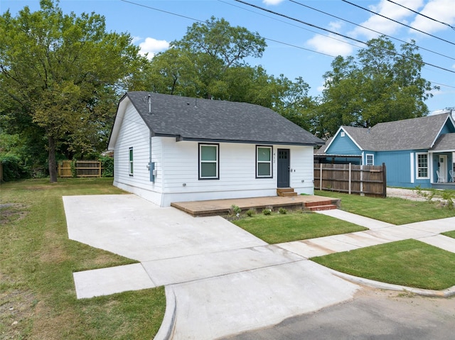 view of front of property featuring fence, driveway, roof with shingles, and a front lawn