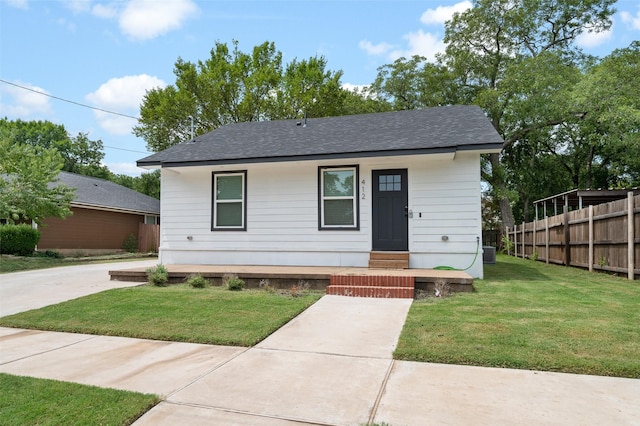 bungalow-style house with fence, a shingled roof, and a front lawn