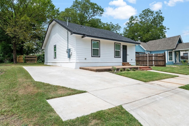 ranch-style home with roof with shingles, fence, a front yard, and concrete driveway