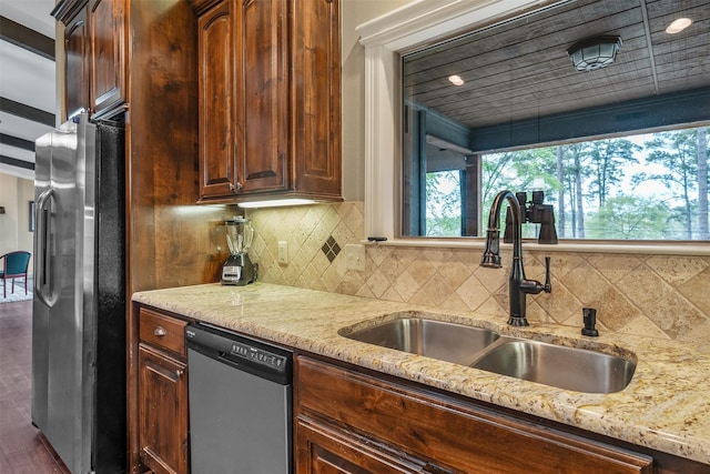 kitchen with backsplash, appliances with stainless steel finishes, a sink, light stone counters, and dark wood-style floors