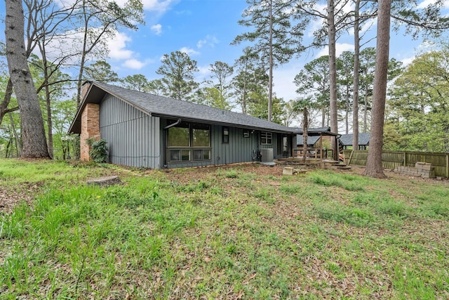 back of house with board and batten siding, fence, roof with shingles, and cooling unit