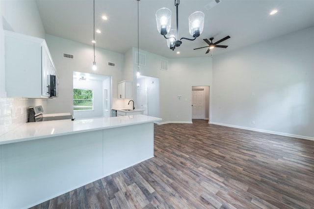 kitchen featuring appliances with stainless steel finishes, a sink, a peninsula, a towering ceiling, and visible vents