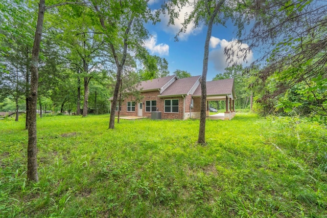 rear view of property featuring brick siding, a lawn, central air condition unit, and a carport