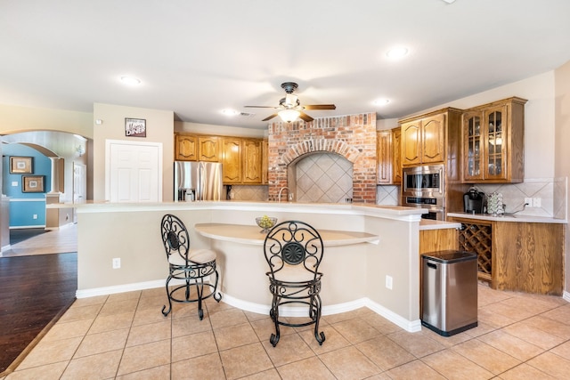 kitchen featuring a ceiling fan, glass insert cabinets, a kitchen breakfast bar, arched walkways, and stainless steel appliances