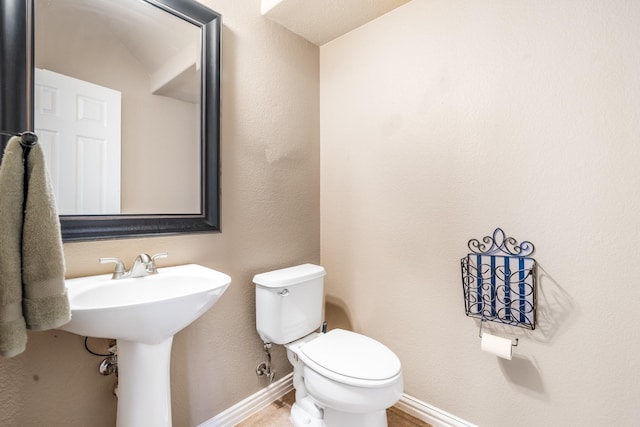 half bathroom with toilet, baseboards, and a sink