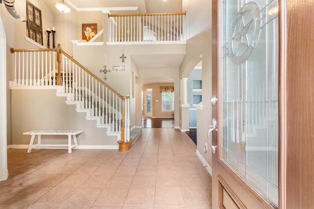 entrance foyer featuring arched walkways, stairs, a towering ceiling, and light tile patterned floors