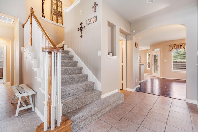 tiled foyer with stairway, arched walkways, baseboards, and visible vents
