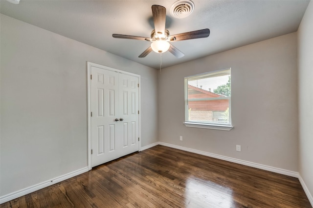 unfurnished bedroom with baseboards, a ceiling fan, dark wood finished floors, and visible vents