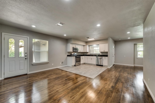 kitchen featuring appliances with stainless steel finishes, white cabinetry, open floor plan, baseboards, and wood finished floors