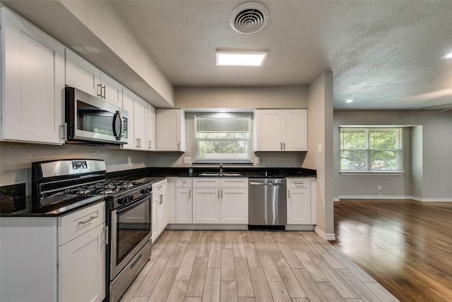 kitchen with visible vents, appliances with stainless steel finishes, light wood-type flooring, a sink, and white cabinets