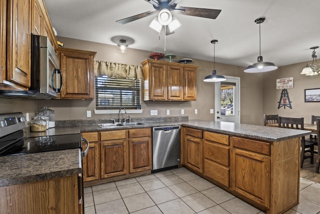 kitchen with dark countertops, brown cabinets, a sink, a peninsula, and stainless steel appliances