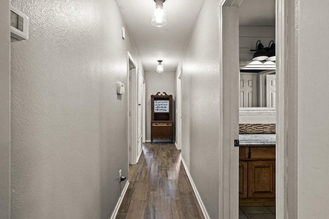 hall featuring baseboards, a textured wall, and dark wood-style floors