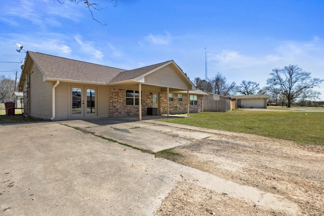 back of house with a shingled roof, brick siding, concrete driveway, french doors, and a lawn