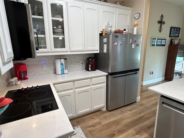 kitchen with appliances with stainless steel finishes, light wood finished floors, white cabinetry, backsplash, and glass insert cabinets