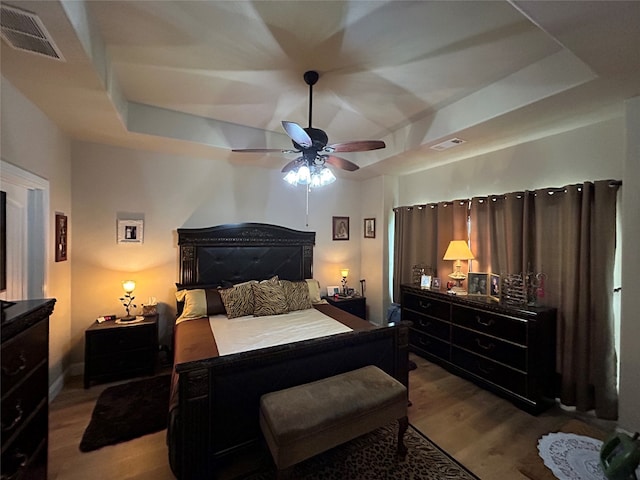 bedroom with a ceiling fan, a tray ceiling, wood finished floors, and visible vents