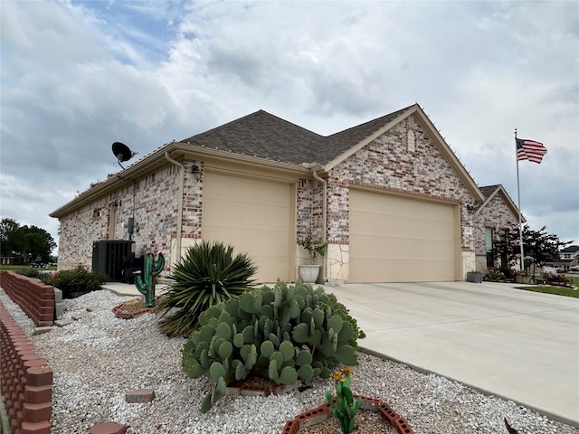 view of home's exterior featuring a shingled roof, an attached garage, brick siding, central AC unit, and concrete driveway