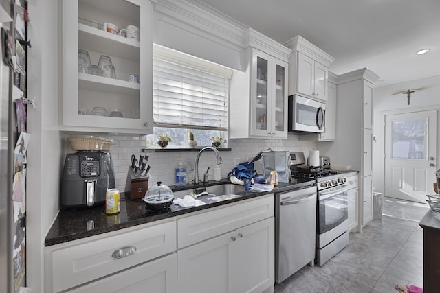 kitchen featuring a sink, dark stone counters, stainless steel appliances, white cabinetry, and backsplash
