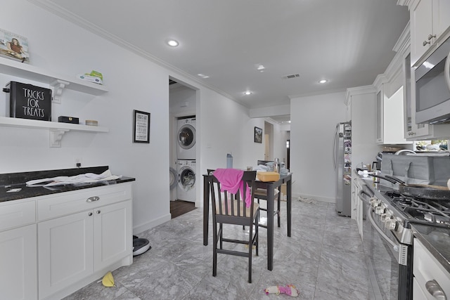kitchen featuring crown molding, stacked washer / drying machine, appliances with stainless steel finishes, white cabinetry, and visible vents