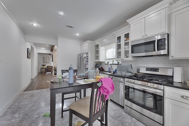 kitchen featuring crown molding, decorative backsplash, glass insert cabinets, a sink, and stainless steel appliances