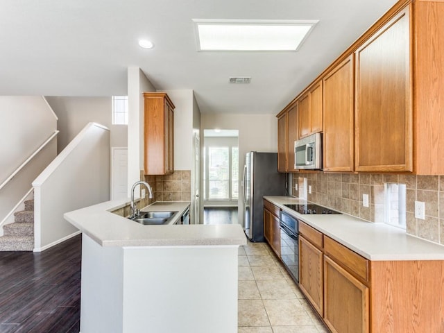 kitchen with visible vents, a peninsula, tasteful backsplash, a sink, and black appliances