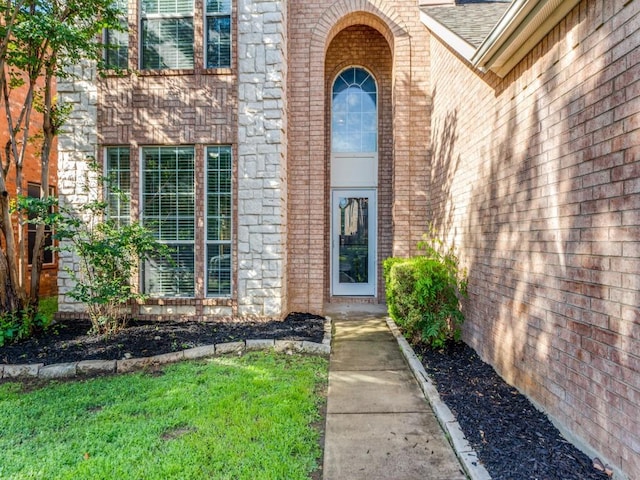 property entrance featuring brick siding and a shingled roof