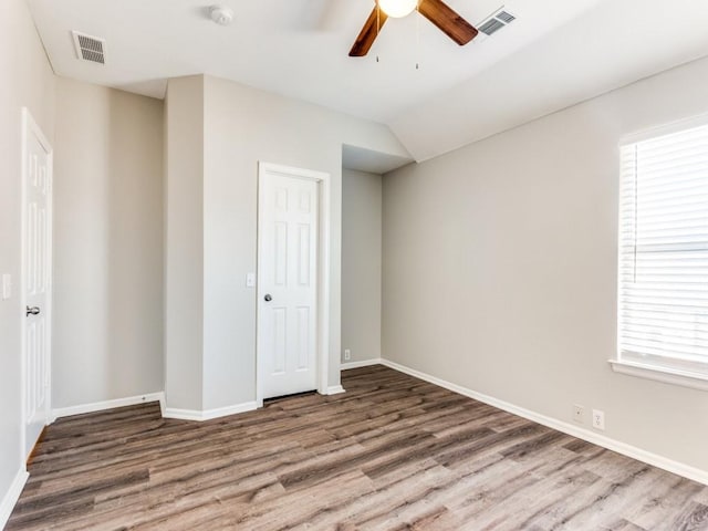 unfurnished bedroom with baseboards, vaulted ceiling, wood finished floors, and visible vents