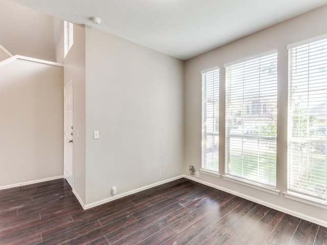 empty room featuring a healthy amount of sunlight, baseboards, and dark wood-style floors